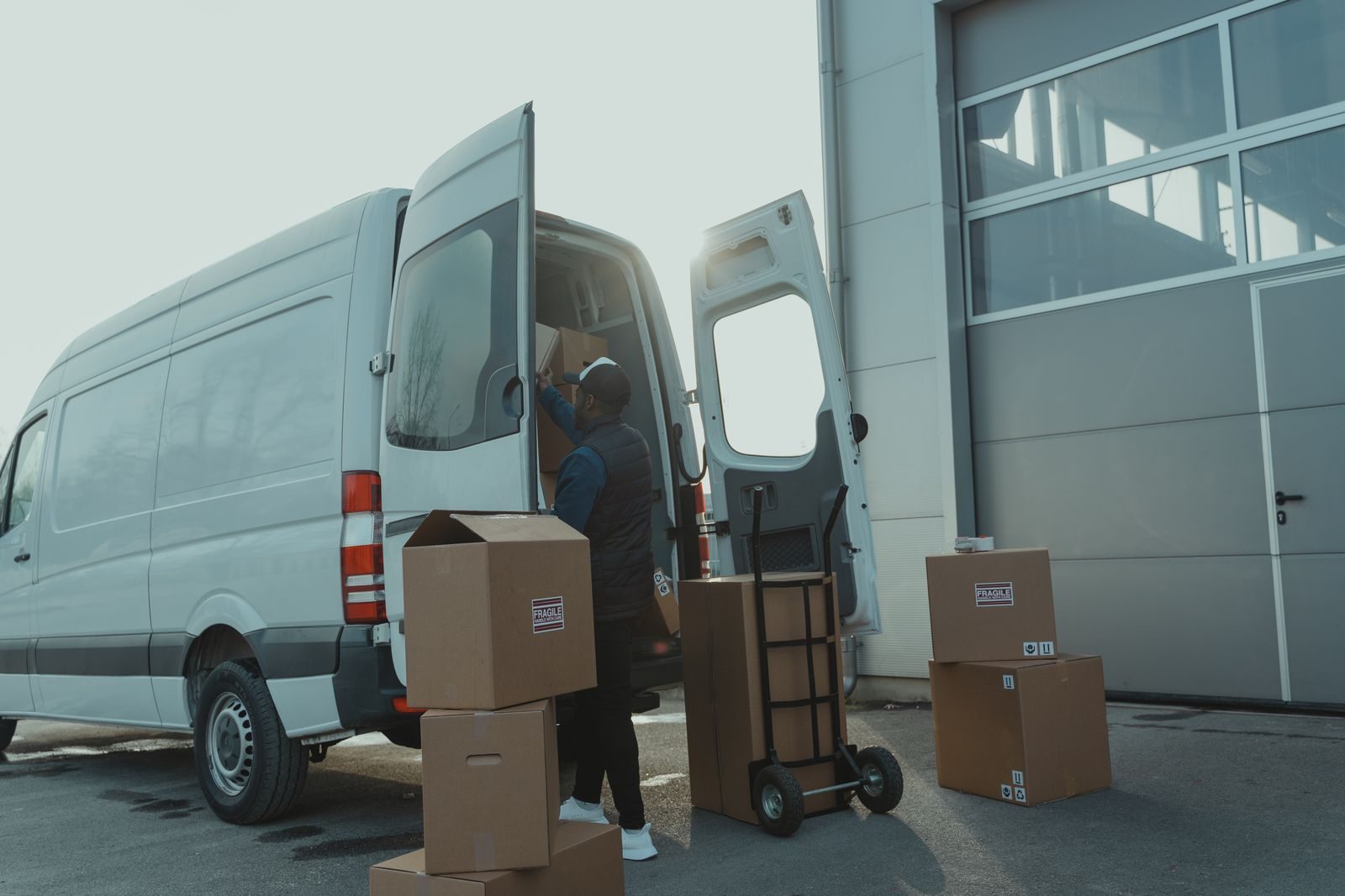 A courier loading boxes into a delivery van outside a warehouse
