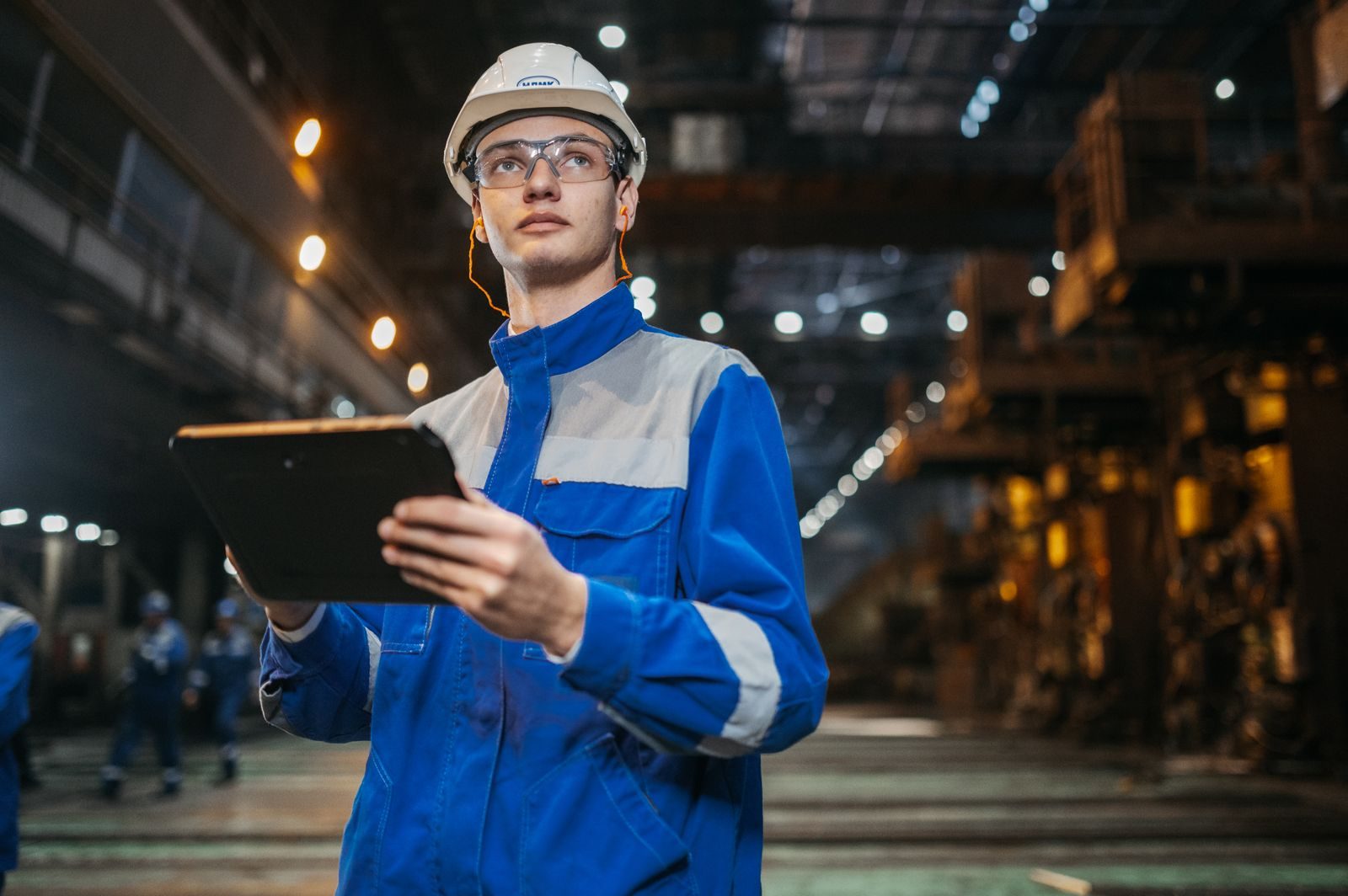 An engineer in safety gear using a tablet on a factory floor