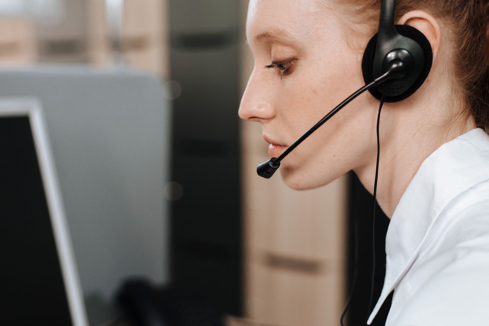 A support agent on a headset working through a ticket at her desk